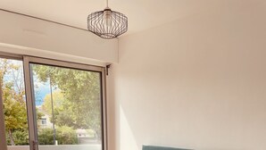 Ein Schlafzimmer mit einem Bett, einem grünen, gepolsterten Kopfende, einem weißen, flauschigen Teppich und Blick ins Freie durch eine Glastür.