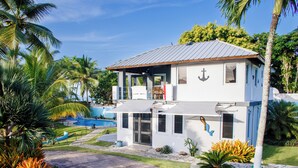 A two-story house with a balcony, a swimming pool, and tropical landscaping. - Luxury Oceanfront Villa Vega Baja: 2 Pools, Waterslide + Tennis/Pickleball court (Vega Baja)
