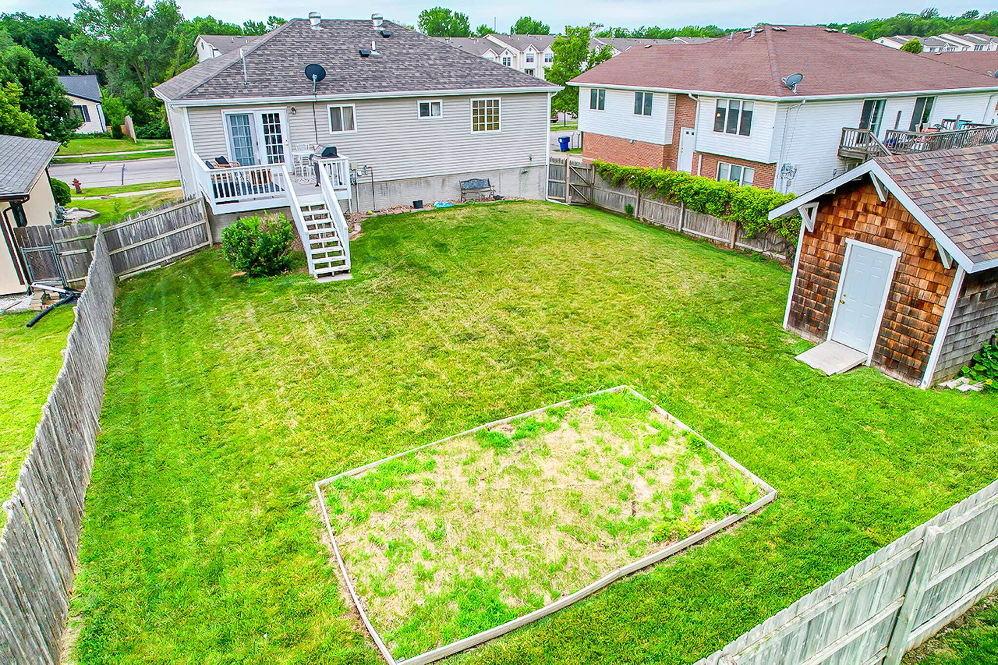 A residential backyard with a lawn, a wooden deck, and a shed.