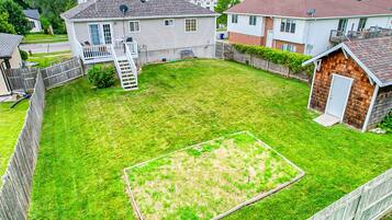 A residential backyard with a lawn, a wooden deck, and a shed.