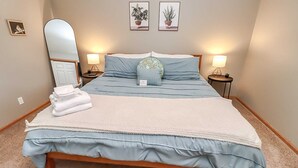 Un letto rifatto con copriletto blu e bianco, due lampade da comodino, uno specchio e due quadri appesi al muro.