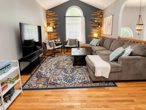 A modern living room with a flat-screen TV, a sofa, a coffee table, and a patterned rug. - Pet-friendly home near UNL with game room (Lincoln)