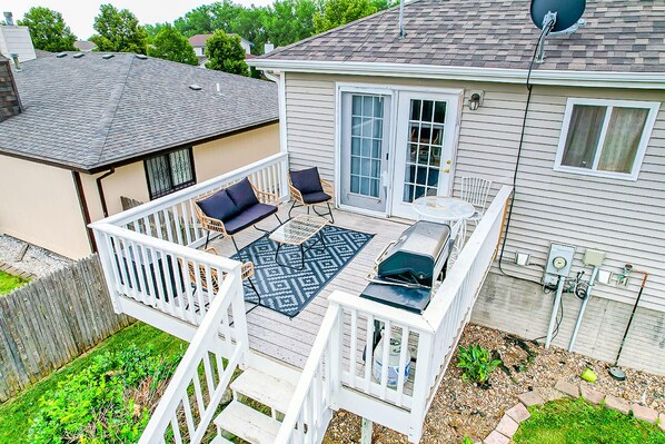 A covered patio with a white railing, two chairs, a small table, and a grill. - Pet-friendly home near UNL with game room (Lincoln)
