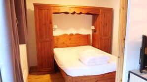 Una cama de madera con un colchón blanco y una toalla doblada, flanqueada por armarios de madera con dos lámparas fijadas a la pared.