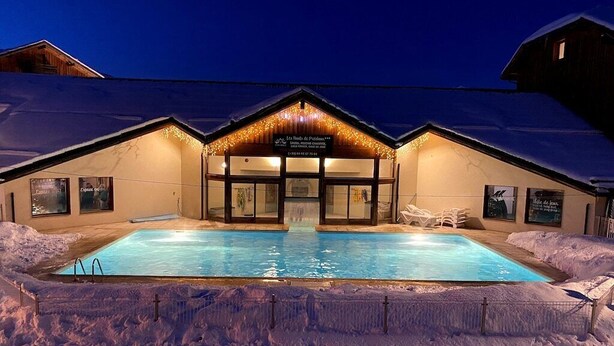 Un hotel con piscina rodeado de nieve, con una entrada iluminada cálidamente y un cartel que indica que es un complejo de esquí.