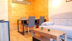 Una habitación acogedora con paredes de madera, una mesa de comedor con sillas, un sofá y una pequeña mesa con una vela verde.