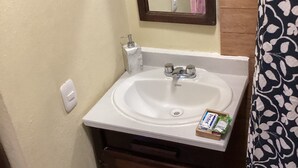 Un baño con un lavamanos blanco, un espejo y un perchero para toallas.