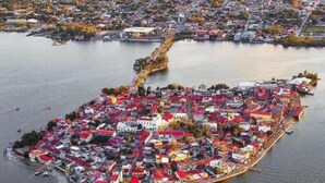Vista aérea de una isla densamente poblada con una mezcla de edificios residenciales y comerciales, conectada al continente por un puente.