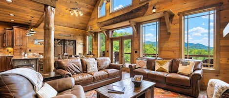 A spacious living area with leather sofas, a coffee table, and a large window offering a view of the outdoors.