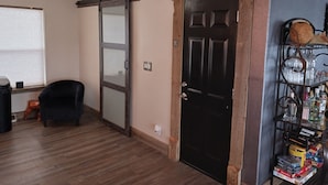 Una habitación con puerta corredera, puerta negra, ventilador de techo, una silla y una estantería con varios objetos.