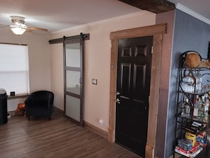 Ein Zimmer mit einer Schiebetür, einer schwarzen Tür, einem Deckenventilator, einem Stuhl und einem Regal mit verschiedenen Gegenständen.