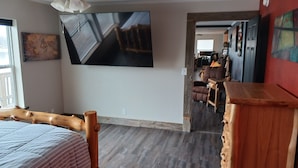 Una habitación con cama, cabecera de madera, ventilador de techo, un cuadro grande en la pared y un aparador de madera.