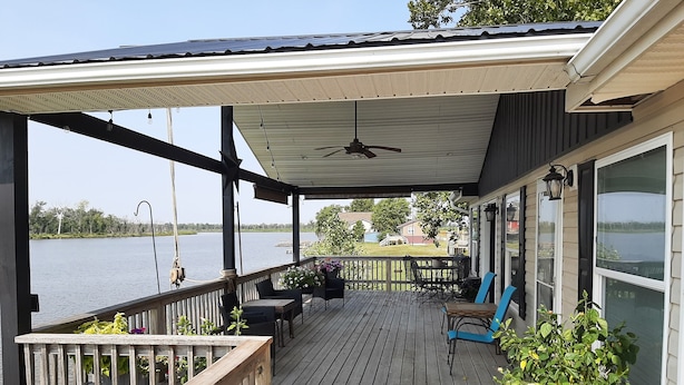 Una terraza techada con mobiliario exterior, un ventilador de techo y vistas a un lago.