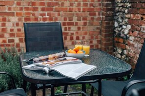 A glass table with a magazine, a bowl of oranges, and two glasses of orange juice. - Honeysuckle Terrace - From 125 Per Night (Henley-on-Thames)