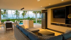 Un salon moderne doté d’un grand téléviseur, de sièges confortables et offrant une vue sur l’océan.