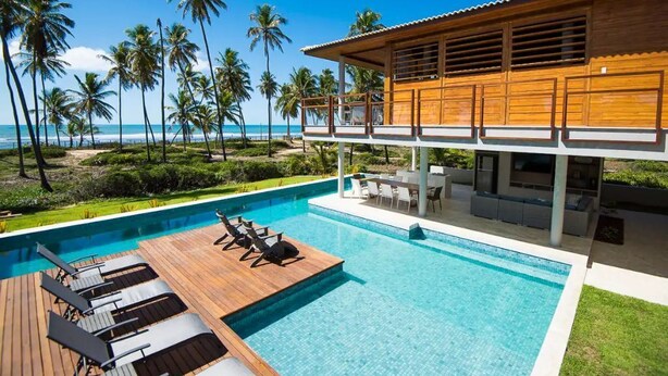 Un espace moderne aménagé au bord de la piscine, avec une terrasse en bois, des chaises longues et une vue sur l’océan.