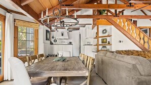 A rustic interior with a wooden dining table, chairs, a sofa, and a staircase.
