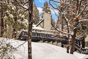 Um edifício coberto de neve com uma chaminé imponente, uma escadaria e uma ponte sobre uma encosta nevada.