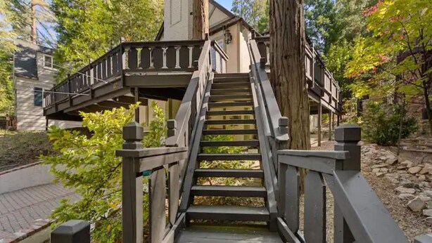 A wooden staircase leading to a house with a porch, surrounded by trees and a stone pathway.