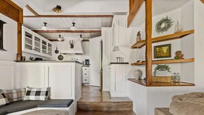 A cozy kitchen with white cabinetry, wooden beams, and a central island.