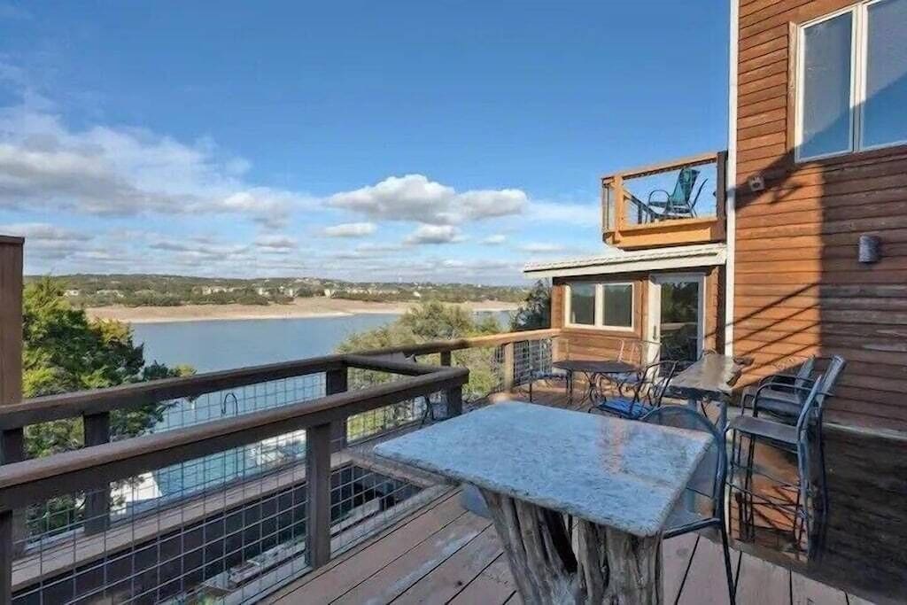 A wooden deck with a stone table and chairs, overlooking a lake.