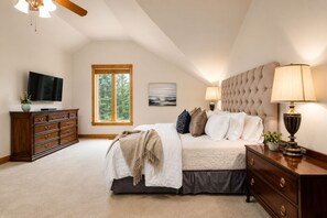 Une chambre à coucher avec un lit, une commode, un téléviseur, une fenêtre et une lampe.