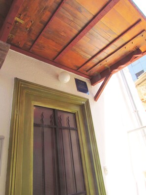 Techo de madera con diseño inclinado, una ventana con marco verde y una celosía decorativa, y una placa en la pared.