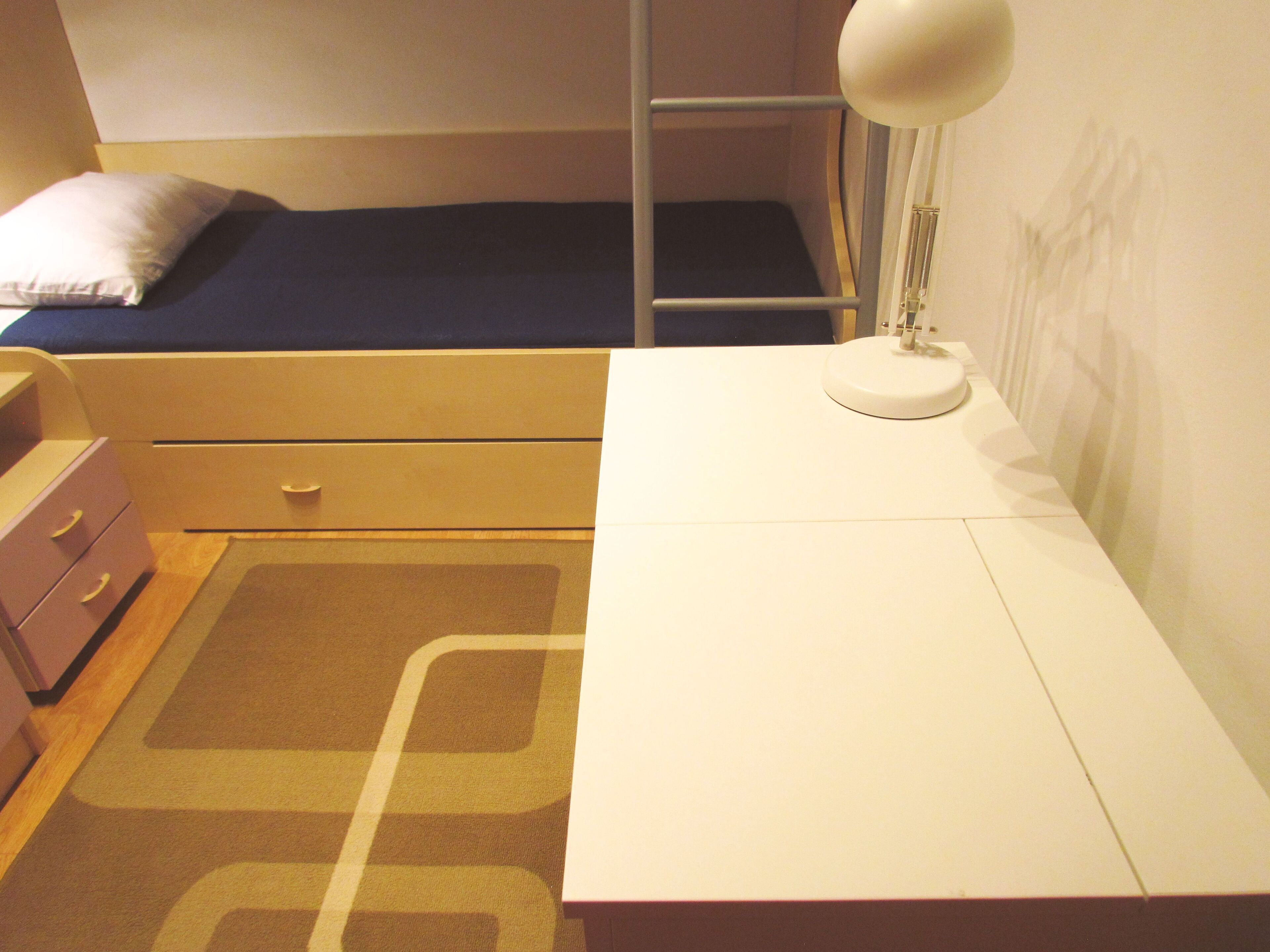Un dormitorio con cama, escritorio, lámpara, cómoda y armario.