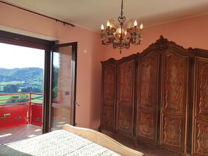 A bedroom with a large wooden wardrobe, a chandelier, and a balcony with a red railing.