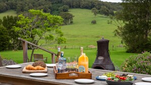 Un coin pique-nique avec de la nourriture, des boissons et une bouteille de jus, installé sur une table en bois donnant sur un champ verdoyant.