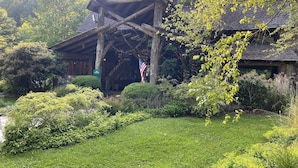 Un chalet rustique en bois, doté d’un porche abrité, entouré d’une végétation luxuriante et d’une pelouse bien entretenue.