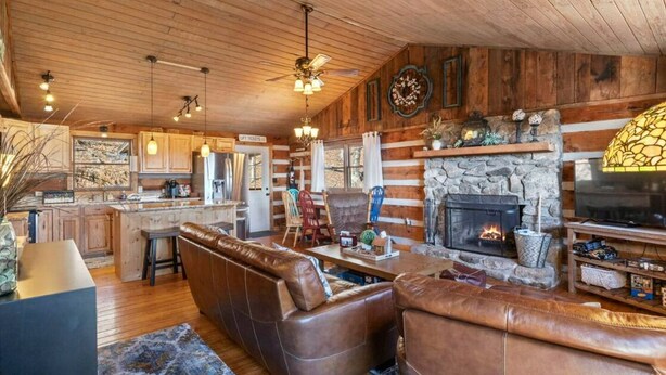 L’intérieur d’un chalet rustique est agrémenté d’une cheminée en pierre, de sièges en cuir, de planchers en bois et d’un coin cuisine.