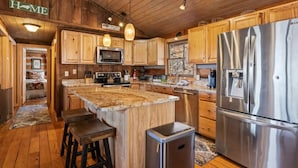 Une cuisine dotée de meubles en bois, d’un réfrigérateur en acier inoxydable, d’un îlot central avec un comptoir en granit et d’un four à micro-ondes.