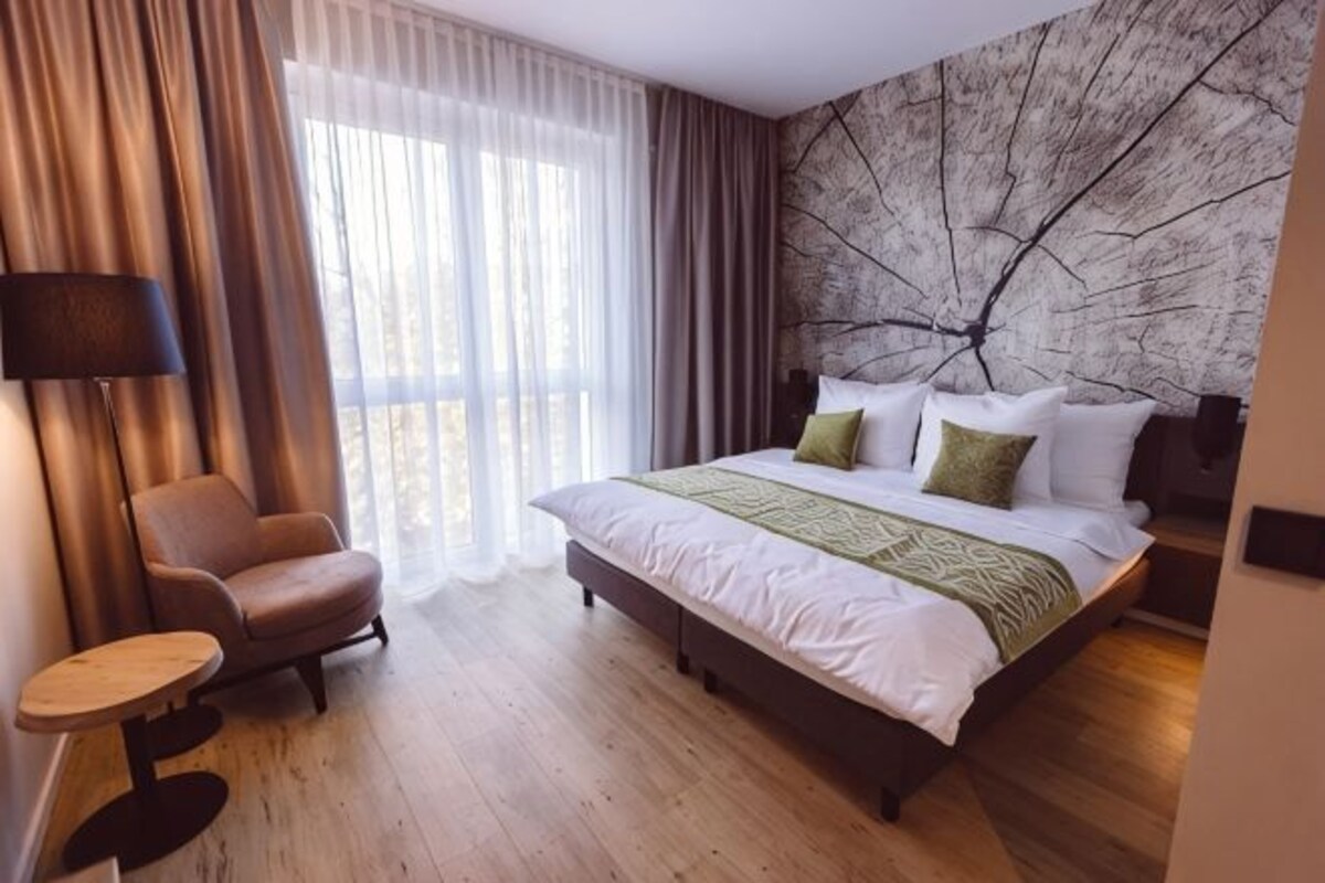 A hotel room with a bed, a chair, a table, and a view of the outdoors.