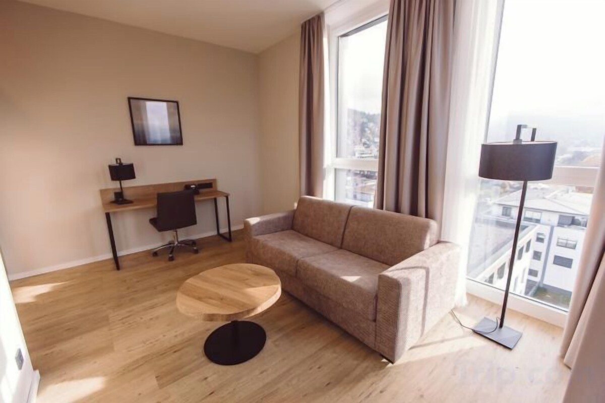 A modern living room with a sofa, a round wooden coffee table, a desk with a chair, and a floor lamp.