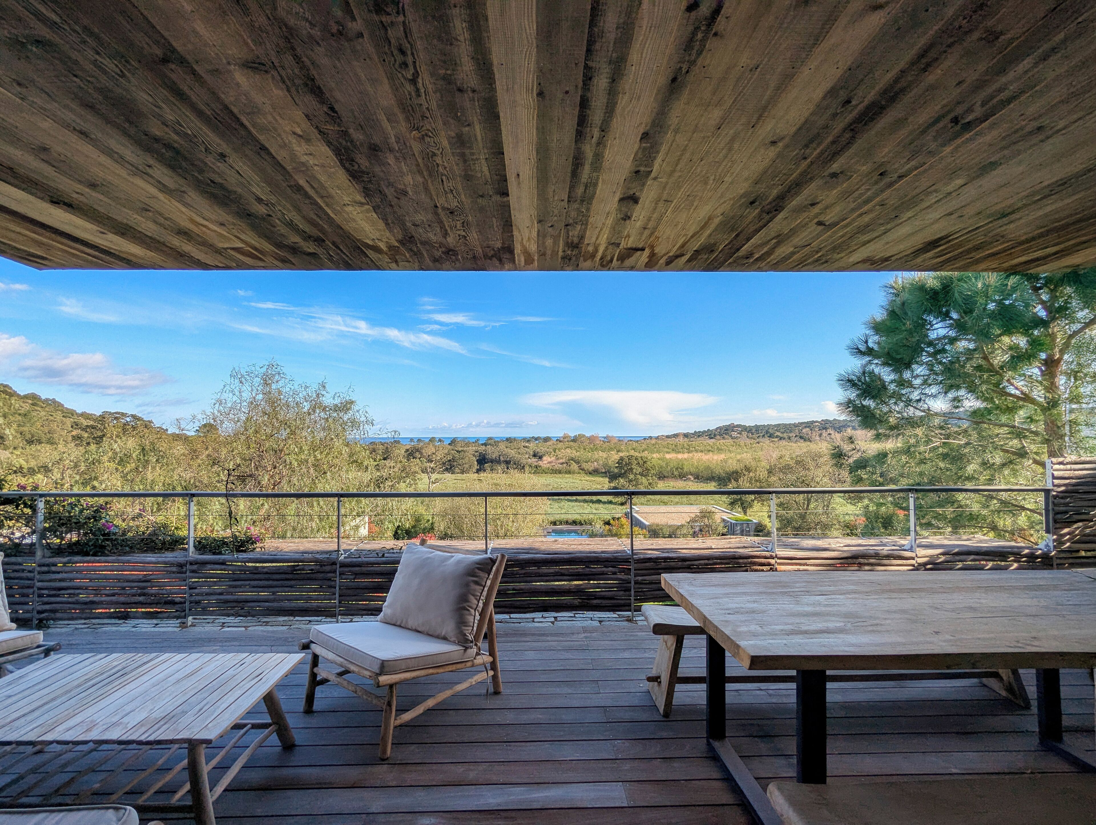 Eine Holzterrasse mit Tisch und Stühlen, mit Blick auf eine malerische Landschaft aus Hügeln und Bäumen.