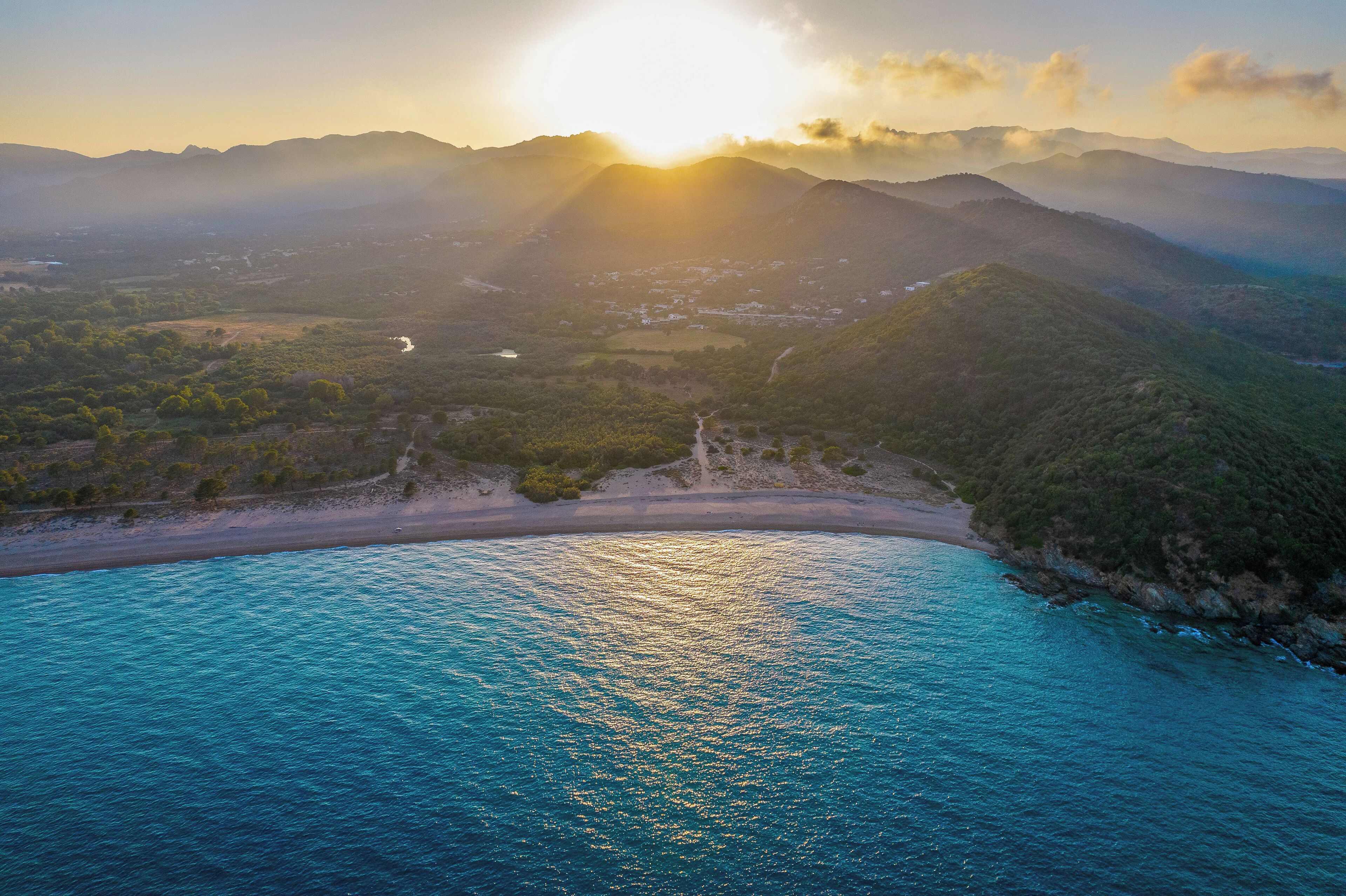 A coastal landscape with a beach, mountains, and a river.