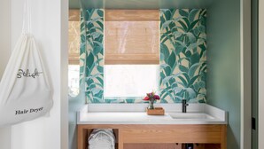A bathroom with a white sink, wooden cabinet, and a window with a bamboo blind.