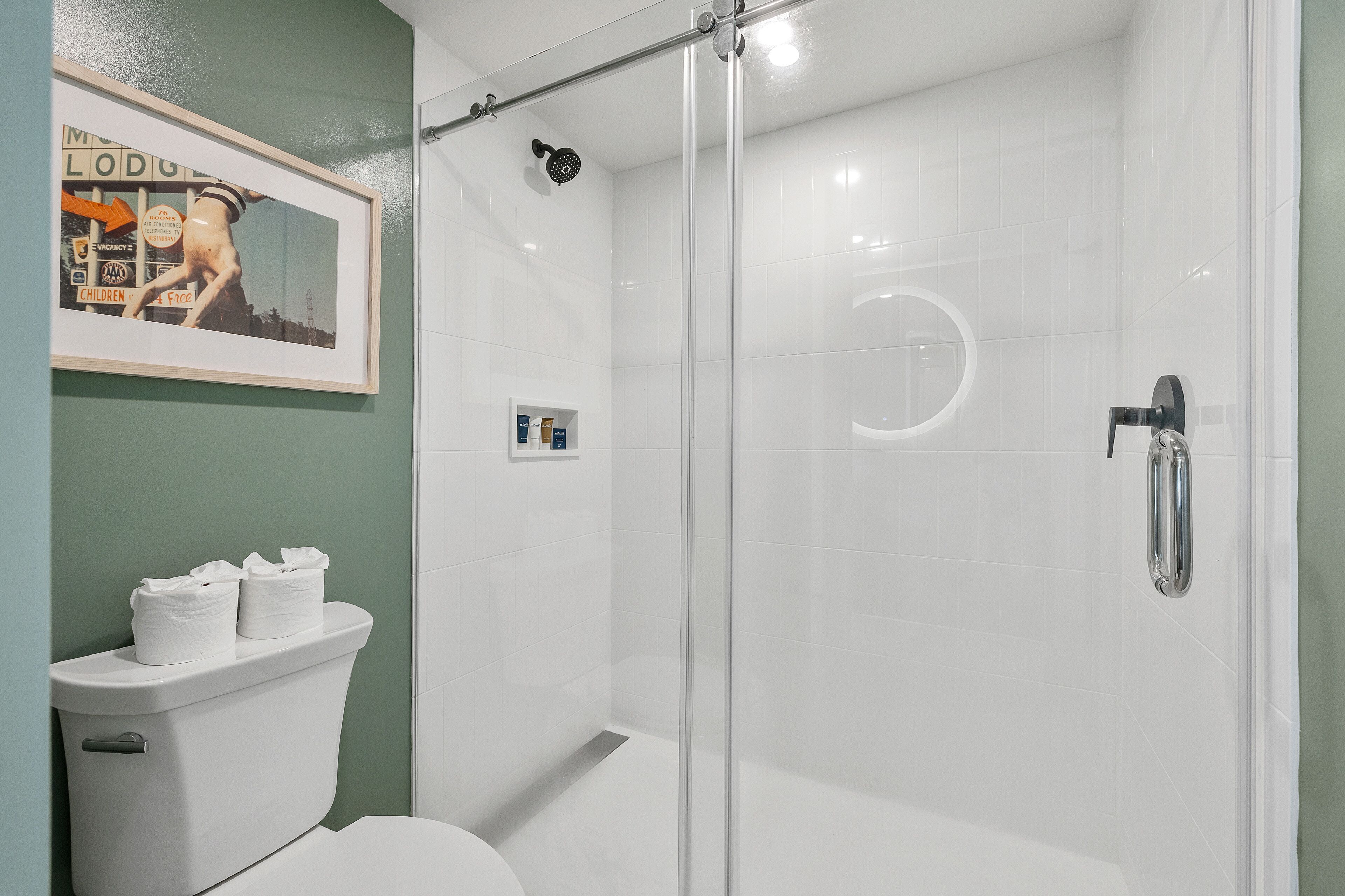 A modern bathroom with a glass-enclosed shower, a toilet with a white tank, and a framed picture on the wall.