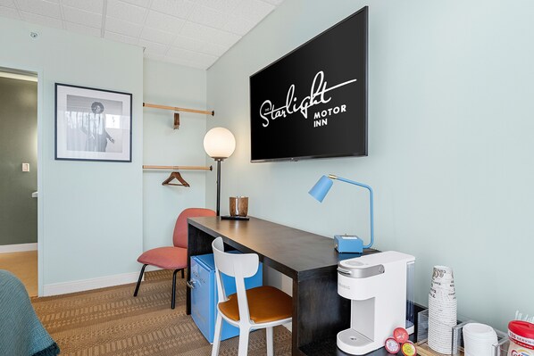 A hotel room with a desk, chairs, a coffee maker, and a television displaying "Starlight Motor Inn" on the wall.
