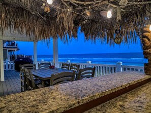 A covered outdoor dining area with a view of the ocean, wooden chairs, a table, and a tiki-style ceiling. - July 11-18 Cancellation Discount! Oceanfront Home with Direct Beach Access! (Myrtle Beach)