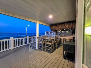 A covered outdoor area with a wooden deck, a table with chairs, a bar area with a thatched roof, and a view of the ocean. - July 11-18 Cancellation Discount! Oceanfront Home with Direct Beach Access! (Myrtle Beach)