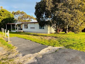 A single-story mobile home with a porch, a paved driveway, and a large tree in the background. - Teddy's Shack  -Pet friendly outside (Robe)