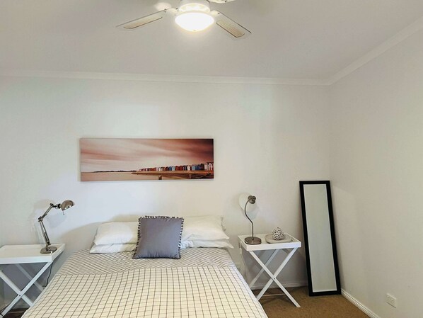 A bedroom with a bed, two bedside tables, a nightstand, a ceiling fan, a wall-mounted light, a mirror, and a painting. - Teddy's Shack -Pet friendly outside (Robe)