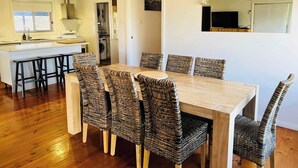 A dining area with a wooden table and wicker chairs, a kitchen in the background, and a large mirror on the wall.