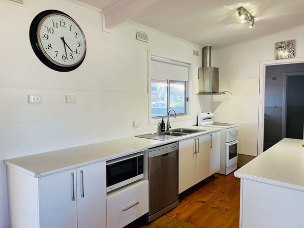 Een moderne keuken met witte kastjes, een roestvrijstalen vaatwasser, een magnetron, een spoelbak en een klok aan de muur.