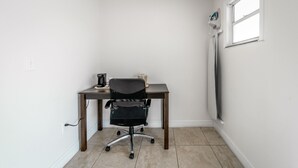 Ein kleiner Büroraum mit Schreibtisch, Stuhl, Kaffeemaschine und einem Fenster.