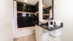Ein modernes Badezimmer mit einer schwarzen Duschkabine, einer weißen Badewanne, einer Arbeitsplatte aus Granit, einem großen Spiegel und ordentlich gefalteten Handtüchern.