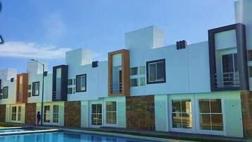 Un immeuble résidentiel moderne doté d’une piscine, avec une façade aux couleurs contrastées, mêlant le blanc et le brun, et un logo comportant le texte « CASA ESTONIA ».
