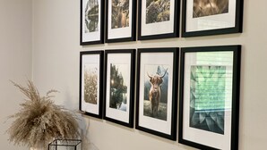 Een muur met meerdere ingelijste foto's, een vaas met gedroogde planten en een kaars in een glazen houder.
